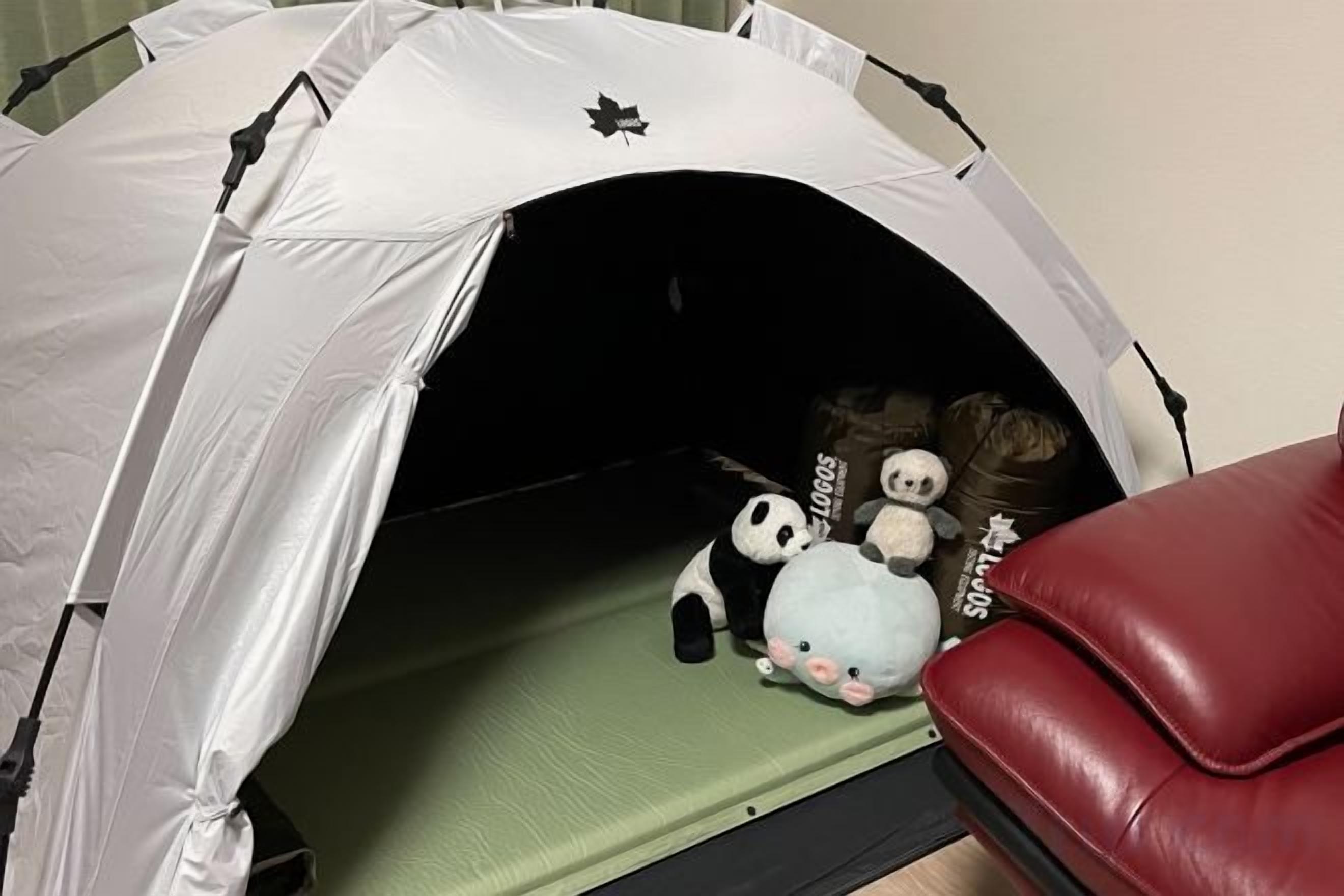 A tent-like structure with a green mat inside, a red chair, and stuffed toys.