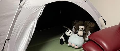 A tent-like structure with a green mat inside, a red chair, and stuffed toys.