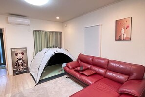 A room with a red leather sofa, a tent-like structure, a framed picture on the wall, and a window with curtains. - Peacock (Osaka)