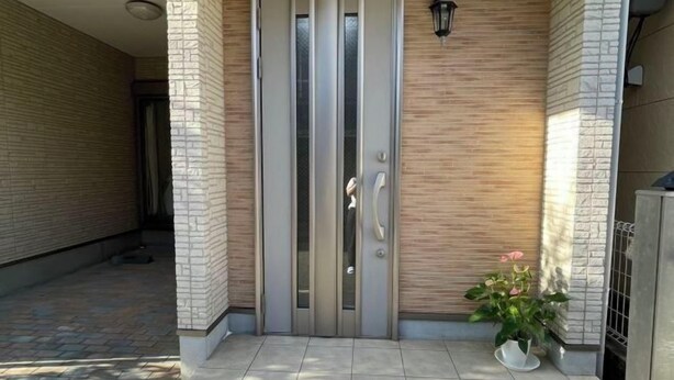 A building entrance with a modern door, a potted plant, and a wall-mounted light fixture. - Peacock (Osaka)