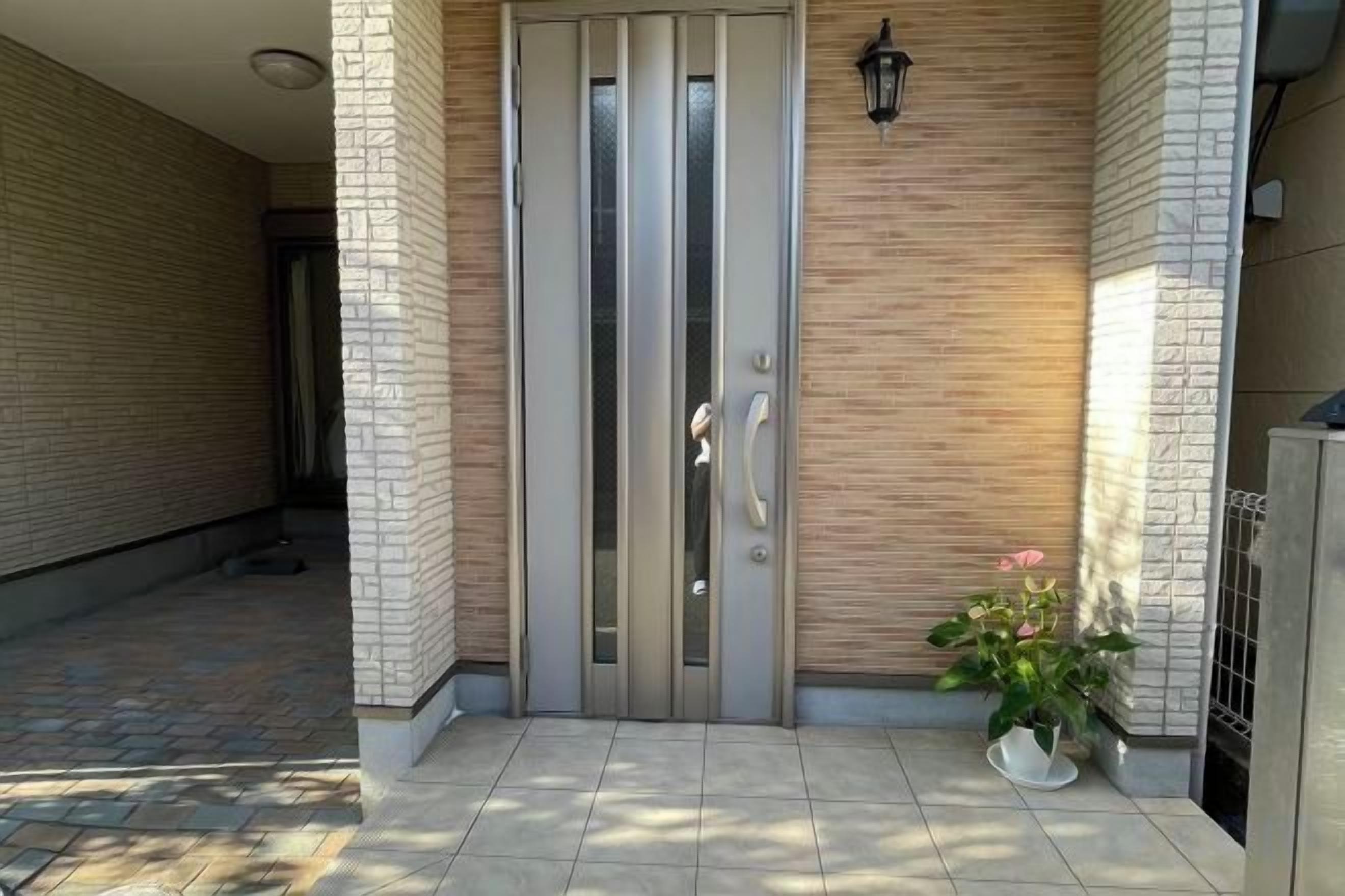 A modern entrance with a glass door, a potted plant, and a wall-mounted light fixture.