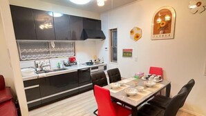 A compact kitchen with black cabinets, a dining table with four chairs, and a red chair. - Peacock (Osaka)