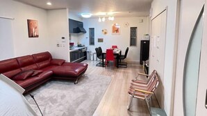 A compact living space with a red leather sofa, a dining table with chairs, a kitchen area, and a small seating area with striped chairs. - Peacock (Osaka)