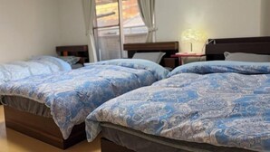 A hotel room with two beds, each with a blue patterned bedspread. There is a window with curtains, a bedside table with a lamp, and a wall-mounted air conditioner. - Peacock (Osaka)