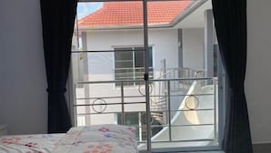 A bedroom with a bed, a window with curtains, and a view of a building with a red roof. - south pattaya soi adam 5 bedrooms pool villa (Pattaya)