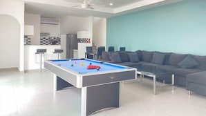 A modern living room with a pool table, a sofa, and a kitchen area in the background. - south pattaya soi adam 5 bedrooms pool villa (Pattaya)