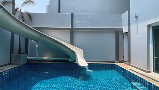 A swimming pool with a slide, surrounded by a white building with a flat roof. - south pattaya soi adam 5 bedrooms pool villa (Pattaya)