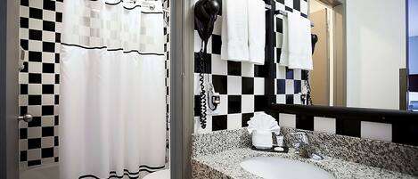 Un baño con cortina de ducha a cuadros, un secador de pelo montado en la pared y un lavabo con encimera de granito.