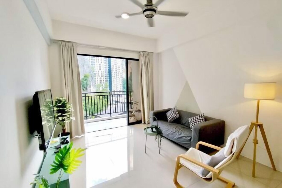 Un salon moderne comprenant un canapé, un fauteuil, un téléviseur, un ventilateur de plafond et un balcon offrant une vue sur les immeubles.