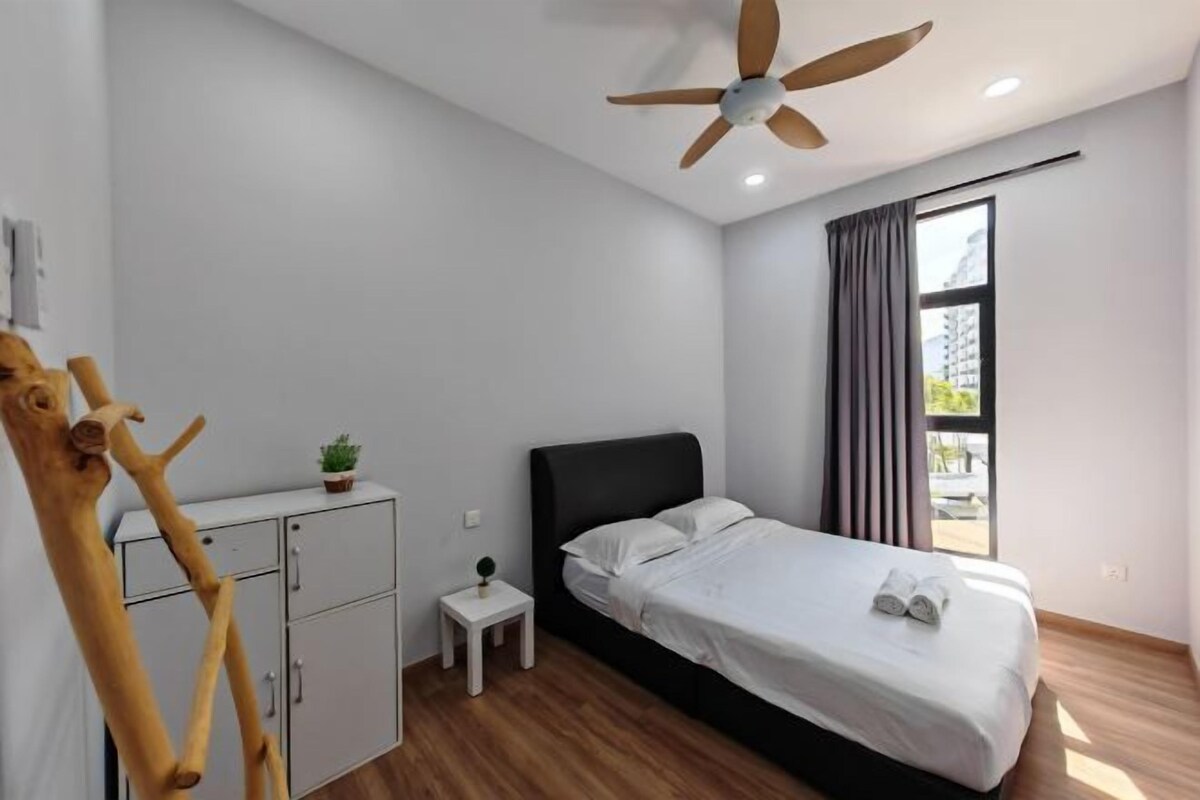 A bedroom with a bed, a ceiling fan, a small bedside table, a nightstand, a wardrobe, and a window with curtains.