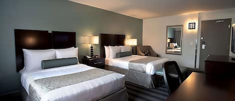 A hotel room with two beds, a desk, and a chair. There are bedside tables with lamps.