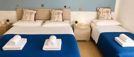 A double room with two beds, each with a blue bedspread and white pillows. There are two nightstands with lamps and a small plant on each.