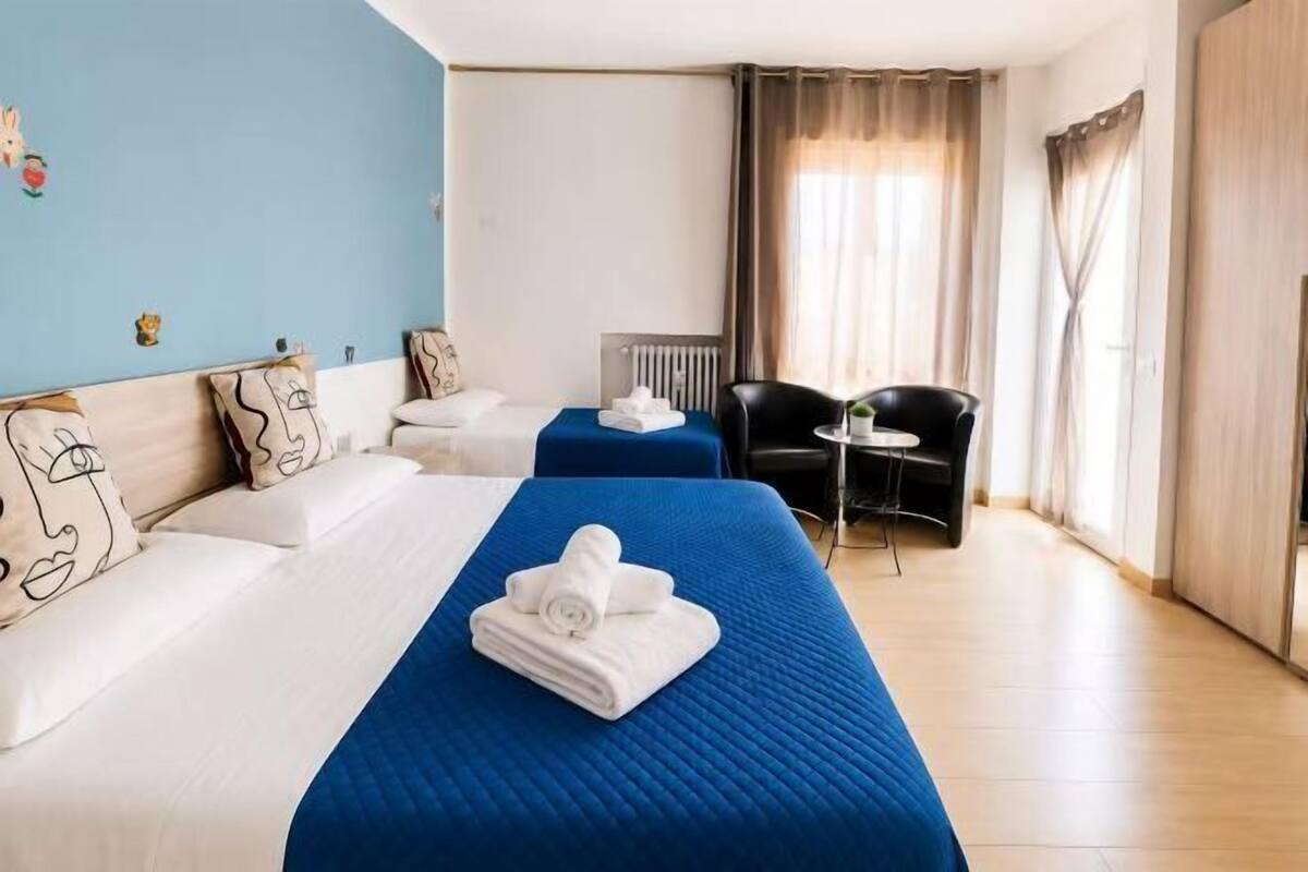 A hotel room with two beds, a desk, a chair, and a view of the city.