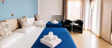 A hotel room with two beds, a desk, a chair, and a view of the city.