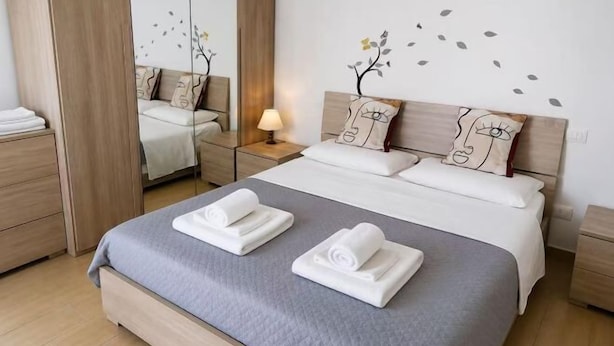 A neatly made bed with towels, a bedside lamp, and a mirror. - huaxia (Venice)