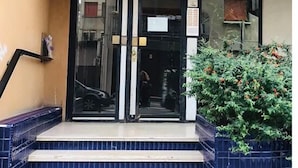 A building entrance with a glass door, a small outdoor seating area, and a sign on the wall. - huaxia (Venice)