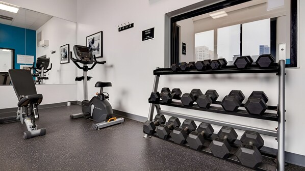 A gym with exercise equipment, including a stationary bike, a rowing machine, and a rack of dumbbells.