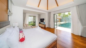 A modern hotel room with a large bed, a TV, a desk, and a view of an outdoor swimming pool. - Anchan Tropicana Pool Villa near Laguna & Beach Phuket Warm Plus (Phuket)