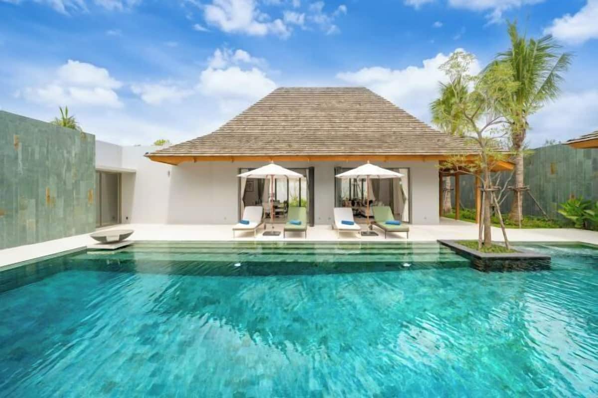 Ein moderner Poolbereich mit Liegestühlen und Sonnenschirmen, ein klares Schwimmbecken und ein Gebäude mit einem Ziegeldach.
