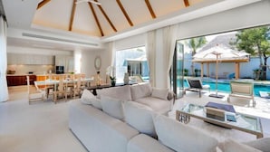 A modern living room with a sofa, a glass coffee table, and a view of a swimming pool. - Anchan Tropicana Pool Villa near Laguna & Beach Phuket Warm Plus (Phuket)
