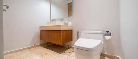 A bathroom with a toilet, a wooden vanity, a mirror, and a light fixture.