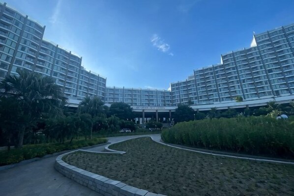 Un hôtel moderne composé de plusieurs immeubles de grande hauteur, doté d’un jardin aménagé et offrant une vue sur un ciel dégagé.
