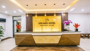 Ein Empfangsbereich im SEN BIEN HOTEL mit modernem Design, einer Kontaktnummer und einer Blumenkomposition.