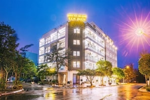 Un hotel de varios pisos con un letrero llamativo, una entrada bien iluminada y un patio con árboles.