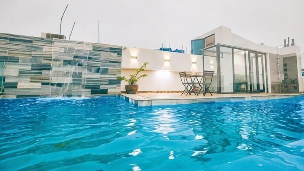 Ein Swimmingpool mit einem modernen Haus im Hintergrund, einer Glastür und einem Stuhl.