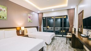 Ein Hotelzimmer mit zwei Betten, einem Schreibtisch, einem Fernseher und einem Balkon mit Vorhängen.