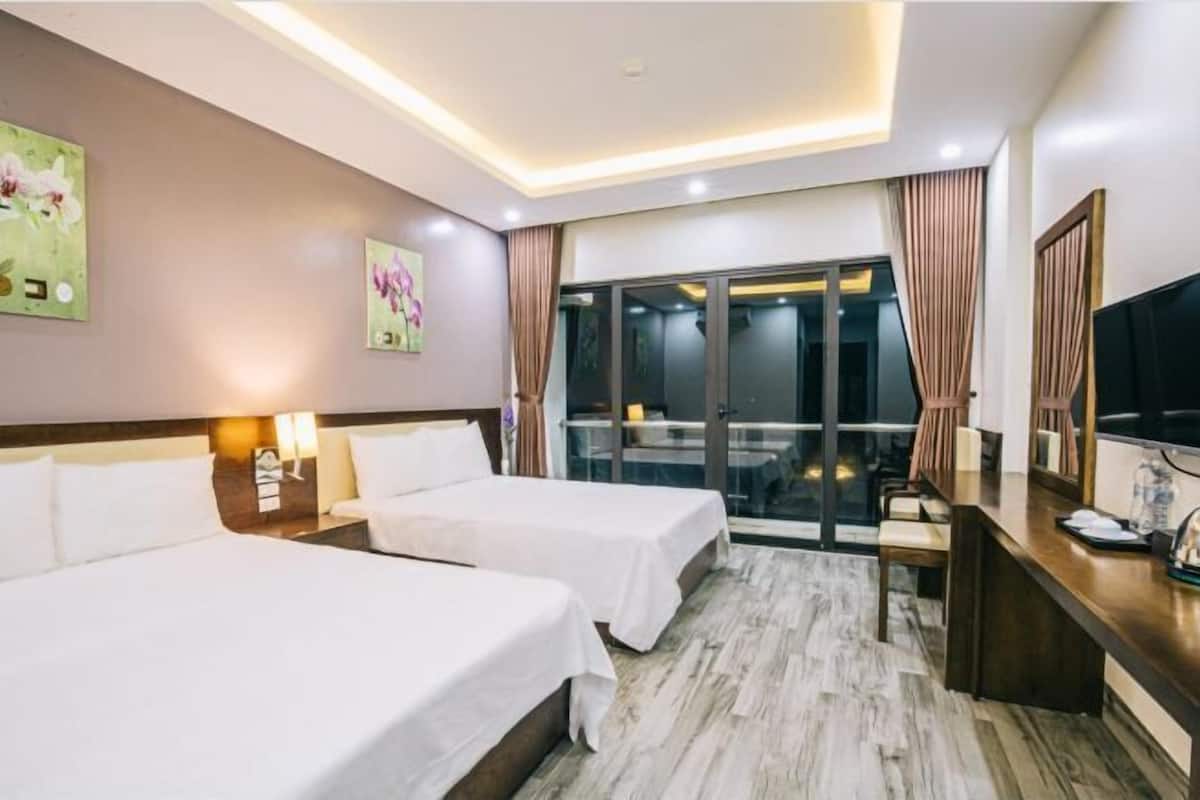 Ein Hotelzimmer mit zwei Betten, einem Schreibtisch, einem Fernseher und einem Balkon mit Vorhängen.
