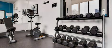 A gym with exercise equipment, including a stationary bike, a rowing machine, and a rack of dumbbells.