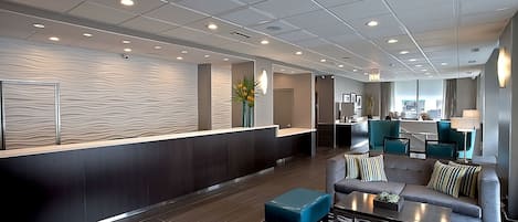 En modern entréhall med en receptionsdisk, en sittgrupp och utsikt över köket.