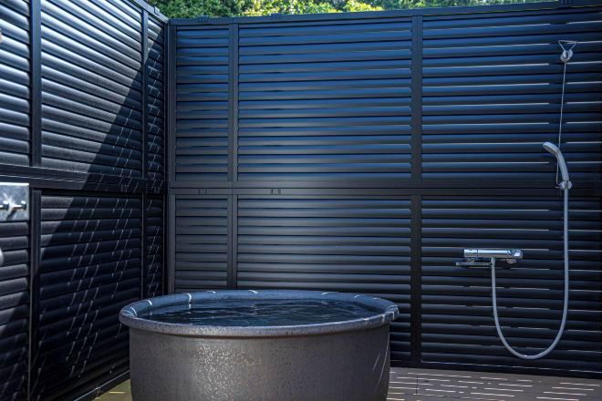 A modern outdoor shower area with a built-in hot tub, a metal faucet, and a hose.