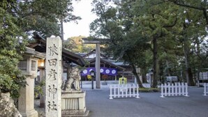 A traditional Japanese gate with stone pillars and a lion statue, leading to a building with a purple roof. - Luxury Trailers Rikyuise (Ise)