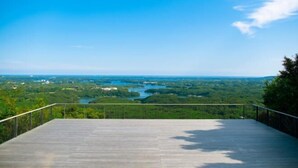 A wooden deck with a metal railing overlooking a river and forested landscape. - Luxury Trailers Rikyuise (Ise)