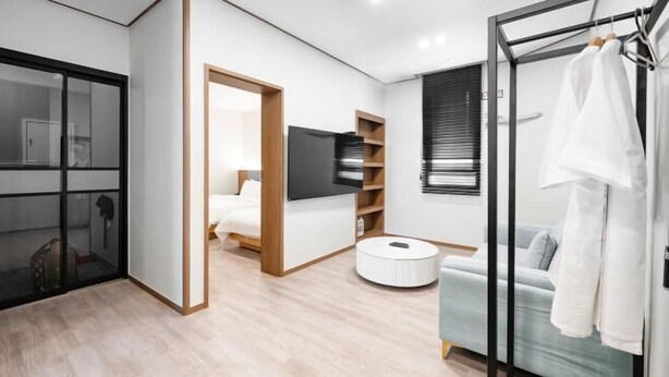 A modern hotel room with a large bed, a TV, a wardrobe, and a seating area with a sofa and a round coffee table. - Hotel signature (Yangsan-si)