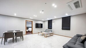 A modern living room with a grey sofa, a dining table with chairs, a coffee table, and a TV mounted on the wall. - Hotel signature (Yangsan-si)