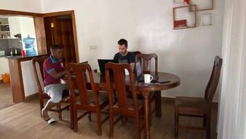 A dining area with wooden chairs and a table, a laptop on the table, and a person sitting at the table.