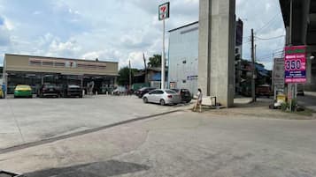 A 7-Eleven convenience store with a gas station in the background, a large concrete pillar, and a signboard with a phone number.
