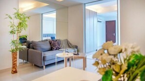 A modern living room with a grey sofa, a small round table, and a large window. - Carlton, Chelsea at Plaza Damas 3, Sri Hartamas by COBNB (Kuala Lumpur)