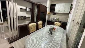 A dining area with a table covered by a lace tablecloth, surrounded by chairs with tufted backs. - Villa Sunrise F1 (Dau)