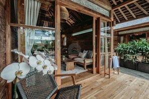 A wooden cabin with a cozy interior, featuring a sofa, a dining table, and a chair. - KAJU Villa Canggu (Bali)