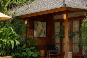 A wooden room with a large abstract painting, a chair, and lush green plants. - KAJU Villa Canggu (Bali)