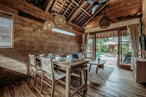A wooden interior with a dining table, chairs, and a view to the outside. - KAJU Villa Canggu (Bali)