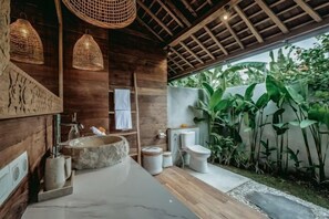 A bathroom with a stone sink, wooden walls, and a view of a garden. - KAJU Villa Canggu (Bali)