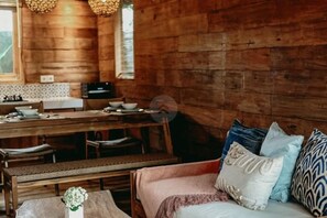 Un interior de madera con comedor, un sofá con cojines estampados y una pequeña mesa con un florero.