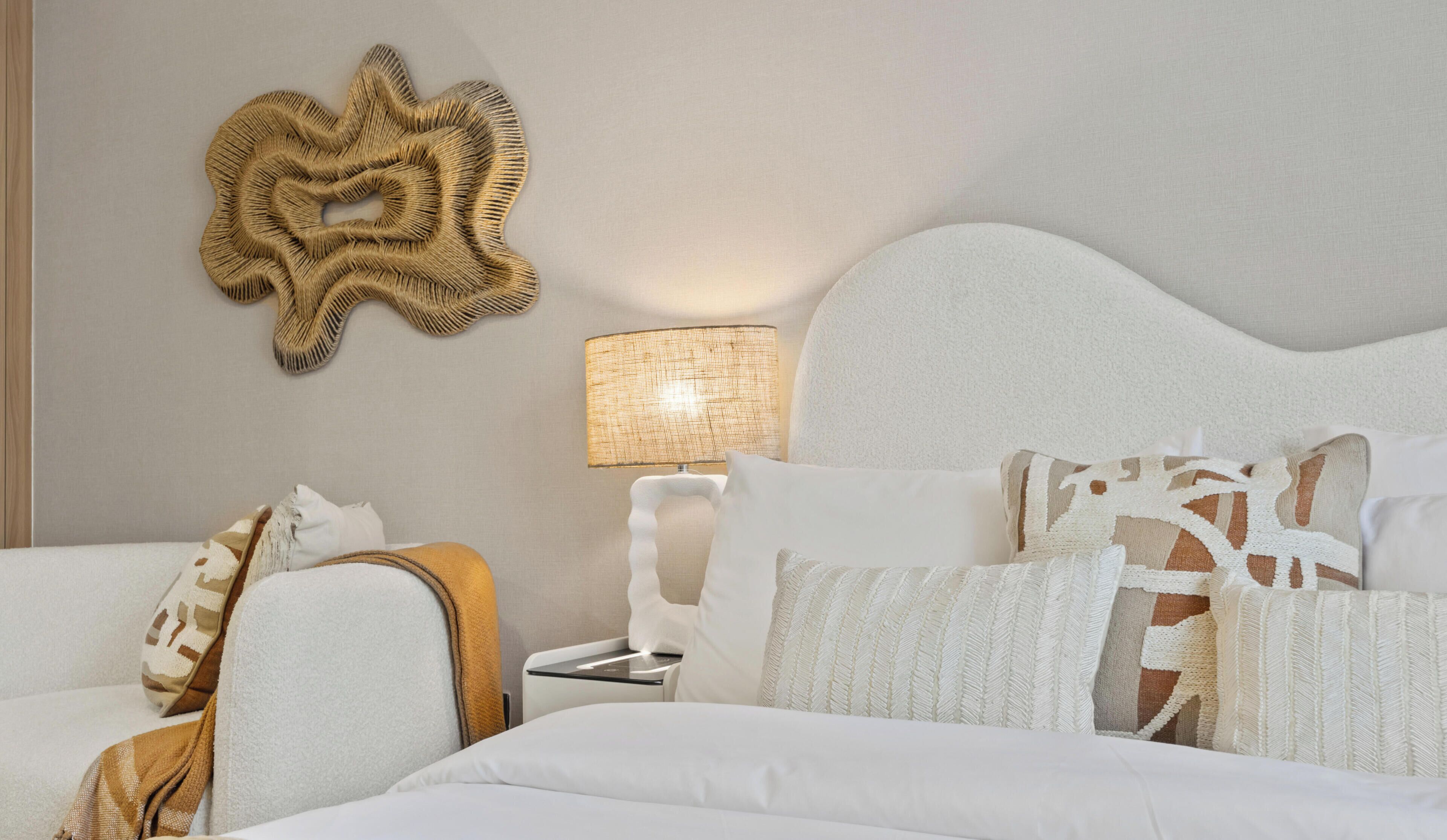 A hotel room with a bed, pillows, a nightstand, a lamp, and a wall art piece.