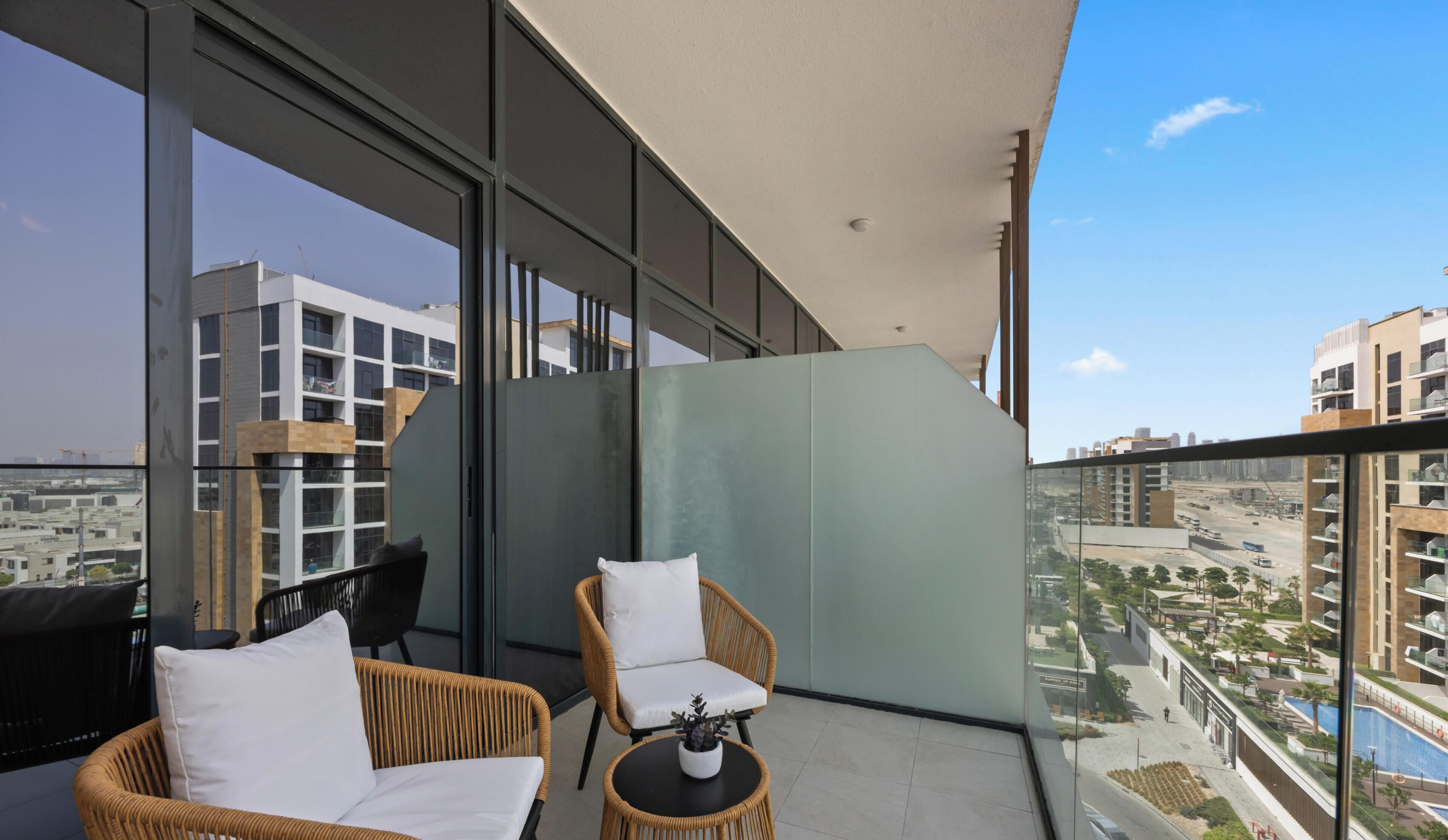 A balcony with wicker chairs and a small table, large windows offering a city view, and a modern building facade.