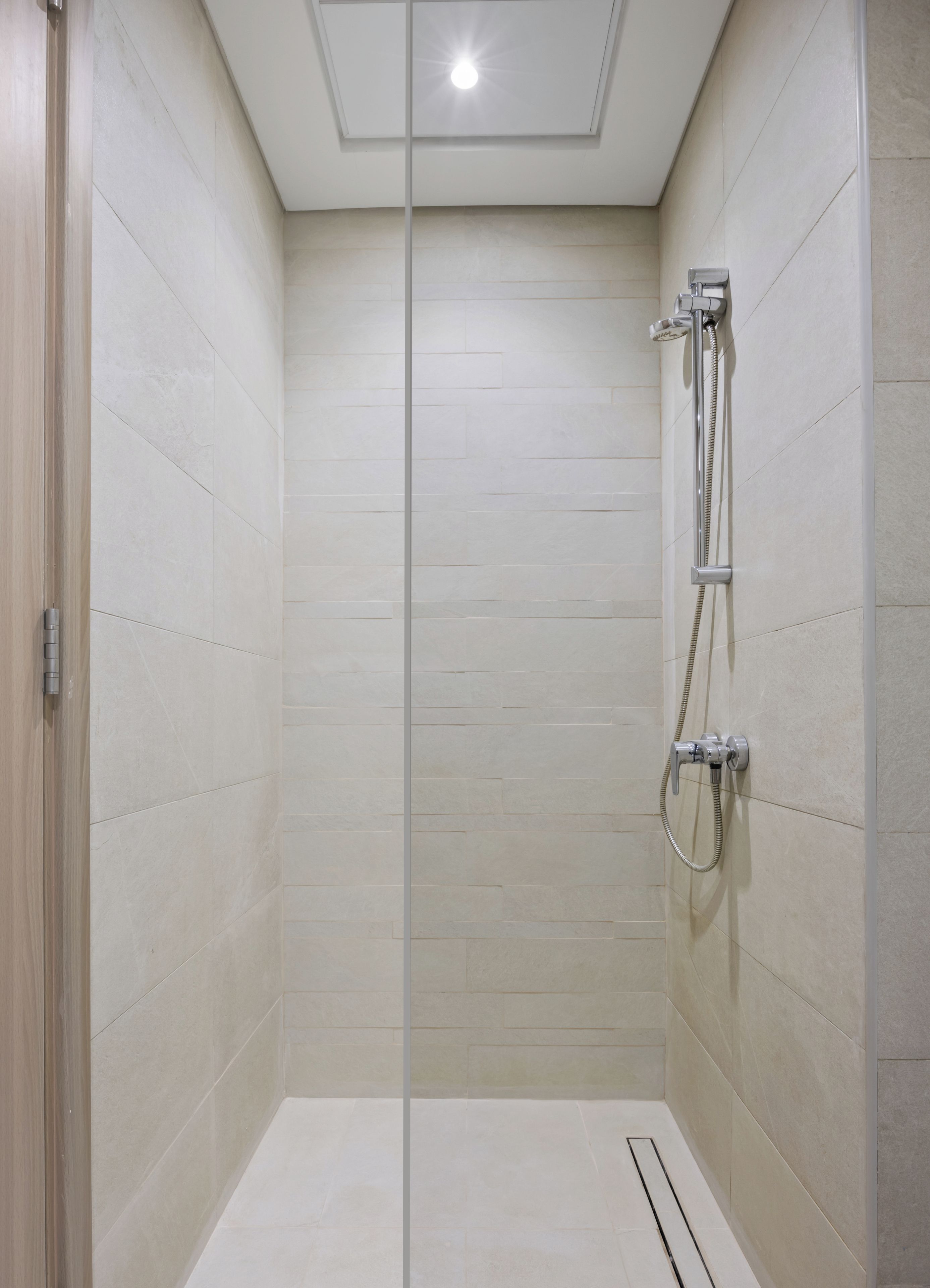 A modern bathroom with a glass shower enclosure, a handheld showerhead, and a wall-mounted faucet.